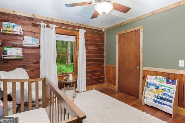 bedroom with wood finished floors, wood walls, and a wainscoted wall