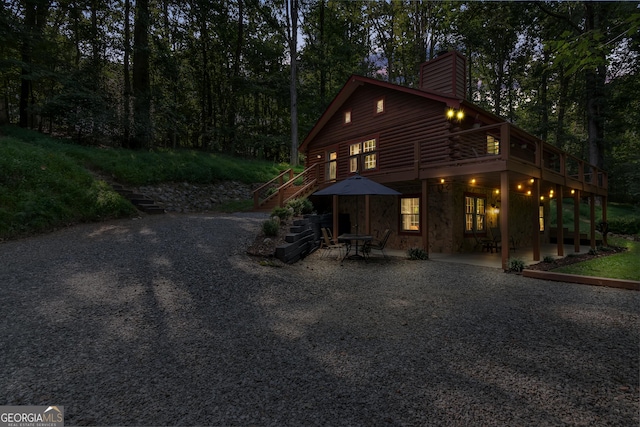 view of front of house featuring stairway, a patio area, a chimney, stone siding, and log siding