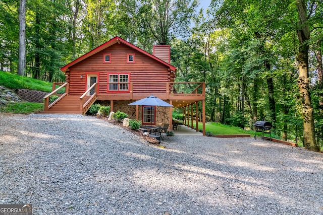 view of front facade with stairs, a chimney, log exterior, and a deck