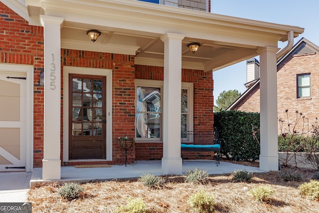 view of exterior entry featuring a porch, a garage, a chimney, and brick siding