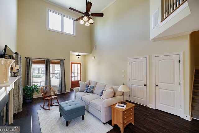 living area with ceiling fan, a fireplace with flush hearth, a towering ceiling, visible vents, and dark wood-style floors