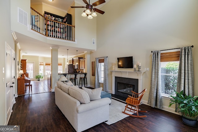 living room featuring a high ceiling, a ceiling fan, baseboards, visible vents, and dark wood-style floors