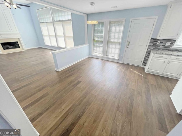 unfurnished living room with baseboards, a ceiling fan, a large fireplace, and dark wood-style floors