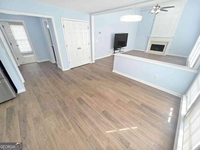 unfurnished living room with a fireplace, wood finished floors, a ceiling fan, and baseboards