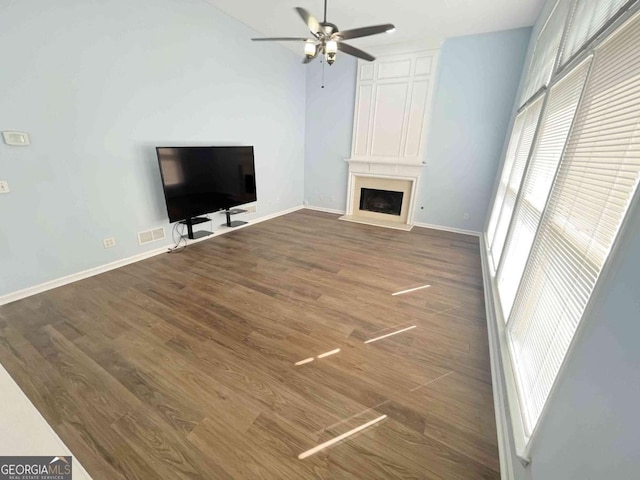 unfurnished living room with a fireplace, plenty of natural light, wood finished floors, and ceiling fan