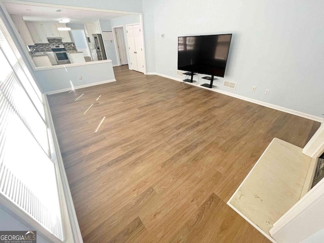 unfurnished living room with wood finished floors, visible vents, and baseboards