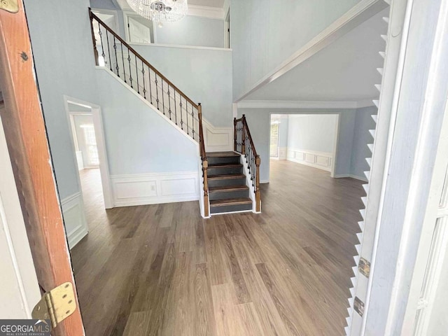 entryway with a towering ceiling, a wainscoted wall, wood finished floors, ornamental molding, and stairs