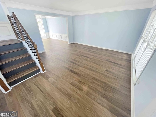 interior space featuring stairway, wood finished floors, ornamental molding, a decorative wall, and wainscoting
