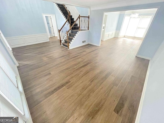 unfurnished living room with wood finished floors, stairs, wainscoting, ornamental molding, and visible vents