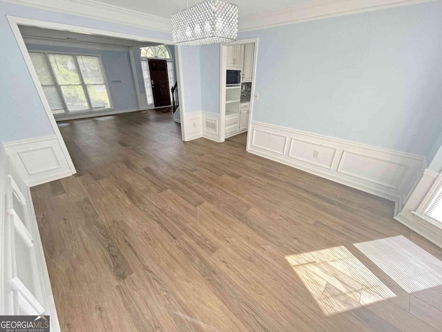 unfurnished dining area featuring a decorative wall, crown molding, wood finished floors, wainscoting, and a chandelier