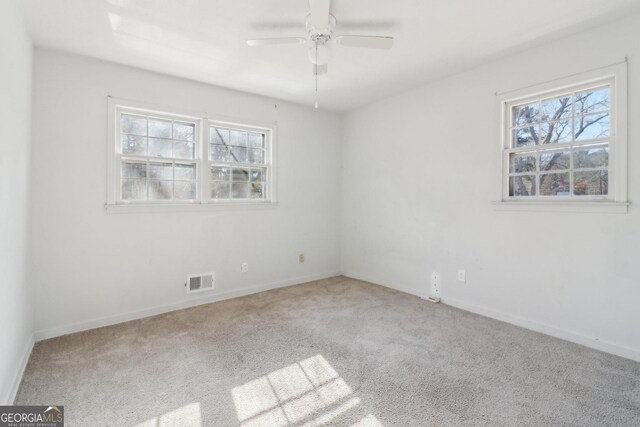 carpeted empty room with a wealth of natural light, a ceiling fan, visible vents, and baseboards