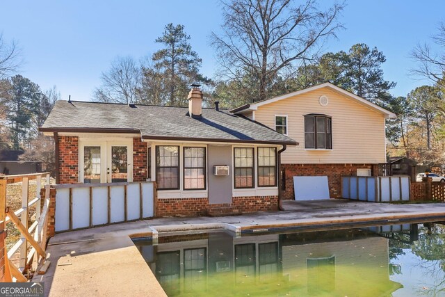rear view of property with brick siding, roof with shingles, and a chimney