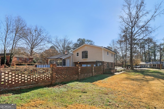 view of property exterior with brick siding, a lawn, and fence