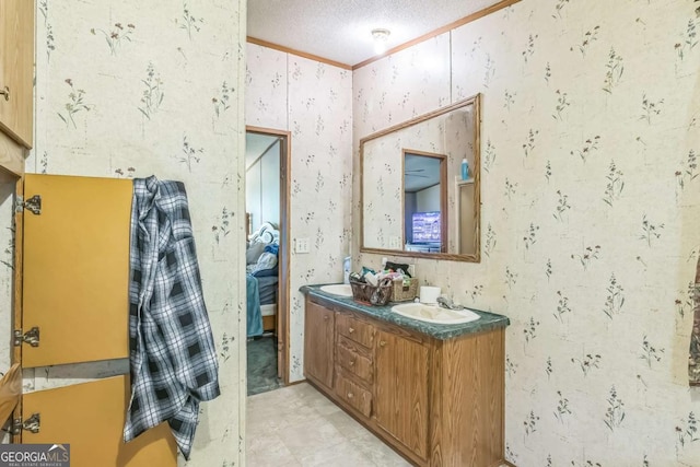 bathroom featuring wallpapered walls, double vanity, ornamental molding, a sink, and a textured ceiling