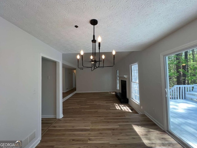 unfurnished dining area featuring wood finished floors, visible vents, baseboards, a textured ceiling, and a notable chandelier