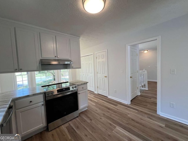 kitchen featuring stainless steel appliances, a textured ceiling, wood finished floors, light countertops, and under cabinet range hood