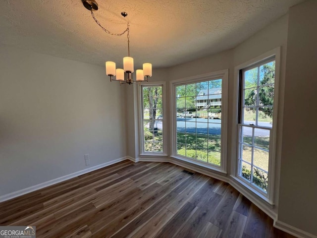 unfurnished dining area with a textured ceiling, an inviting chandelier, visible vents, baseboards, and dark wood-style floors