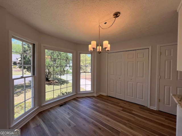 unfurnished dining area with a notable chandelier, visible vents, baseboards, a textured ceiling, and dark wood-style flooring