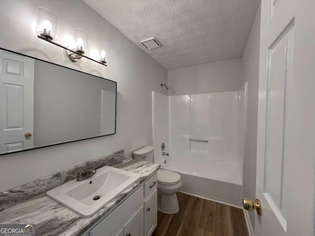full bathroom with wood finished floors, a textured ceiling, vanity,  shower combination, and toilet