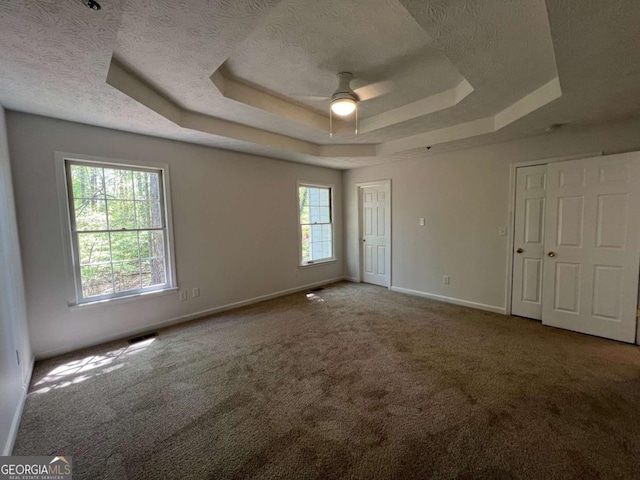 unfurnished bedroom featuring baseboards, carpet floors, a raised ceiling, and multiple windows