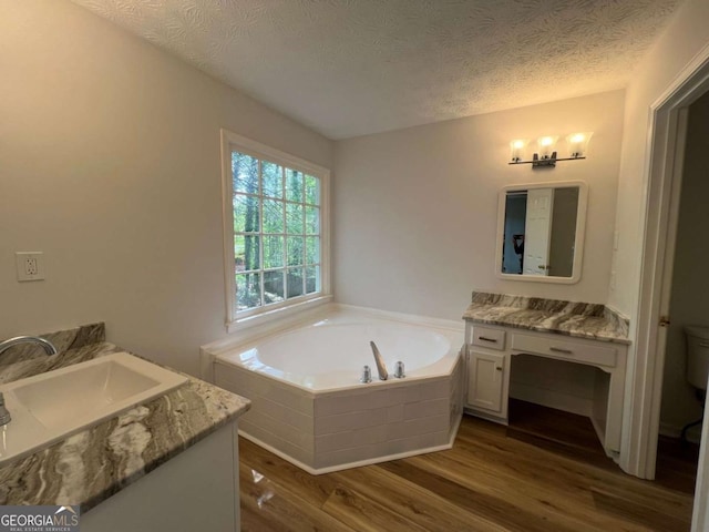full bathroom featuring wood finished floors, toilet, vanity, a bath, and a textured ceiling