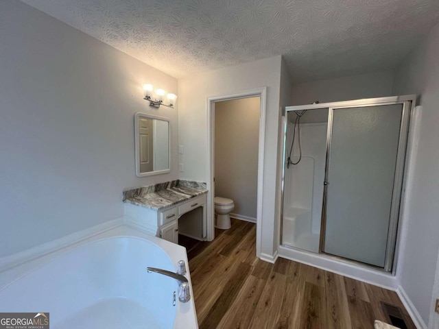 bathroom featuring a shower stall, toilet, wood finished floors, and a textured ceiling