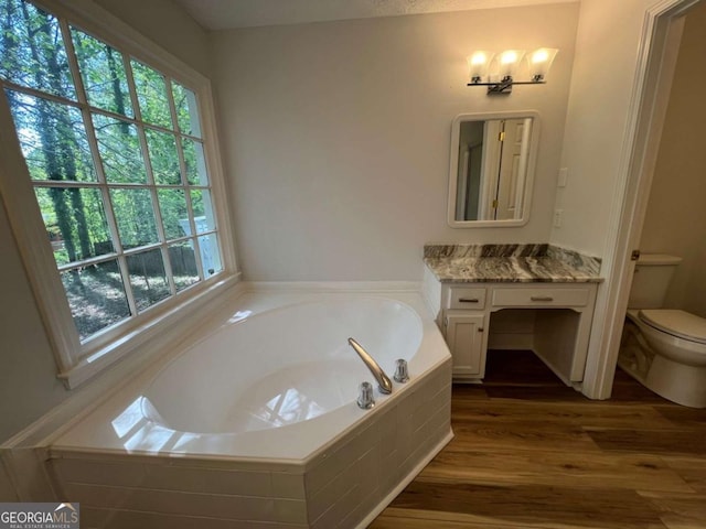 bathroom with a bath, wood finished floors, vanity, and toilet