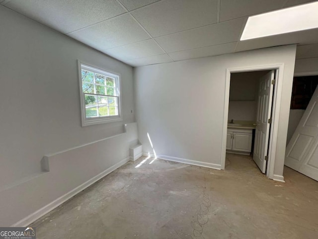 unfurnished bedroom with unfinished concrete floors, a paneled ceiling, ensuite bath, and baseboards