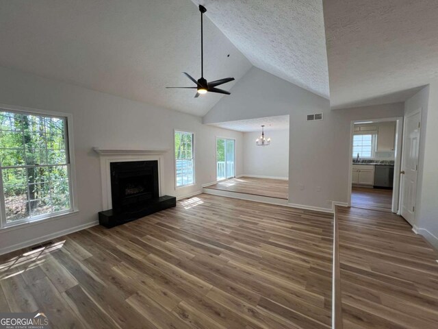 unfurnished living room with wood finished floors, visible vents, a wealth of natural light, and ceiling fan with notable chandelier