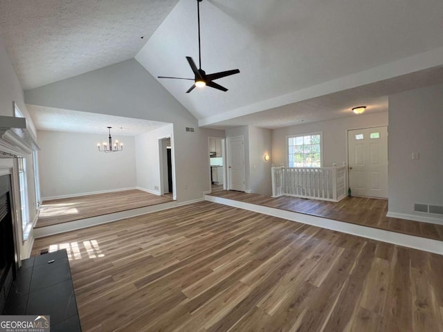 unfurnished living room featuring baseboards, high vaulted ceiling, ceiling fan with notable chandelier, wood finished floors, and a fireplace