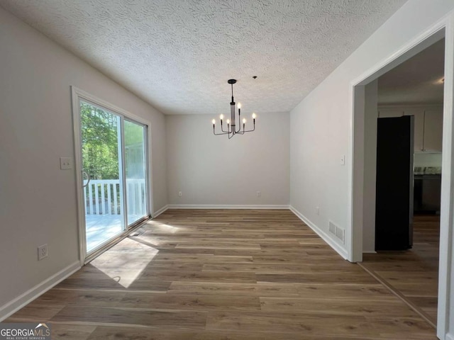 unfurnished dining area with a textured ceiling, visible vents, baseboards, a chandelier, and wood finished floors