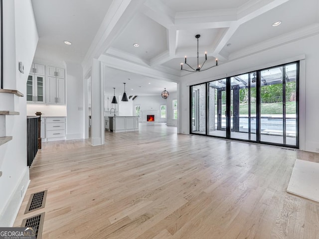 unfurnished living room featuring healthy amount of natural light, a chandelier, light wood-style flooring, coffered ceiling, and beamed ceiling