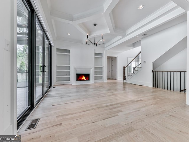 unfurnished living room with built in shelves, healthy amount of natural light, a chandelier, coffered ceiling, and crown molding