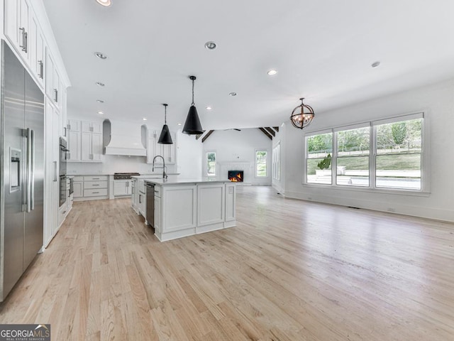 kitchen with open floor plan, appliances with stainless steel finishes, light wood-type flooring, a chandelier, and premium range hood