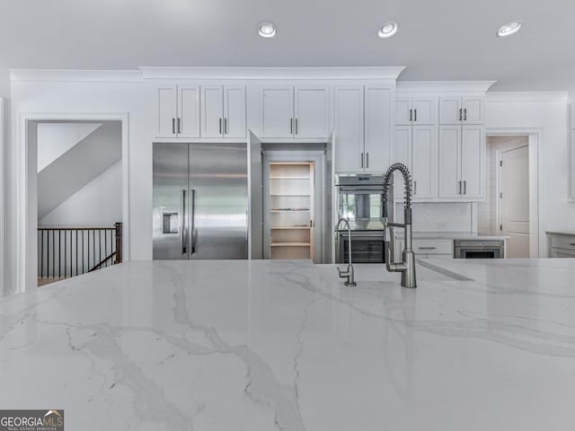 kitchen featuring stainless steel appliances, recessed lighting, white cabinets, light stone counters, and tasteful backsplash