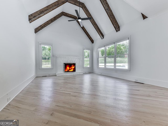 unfurnished living room with plenty of natural light, a lit fireplace, beamed ceiling, high vaulted ceiling, and ceiling fan