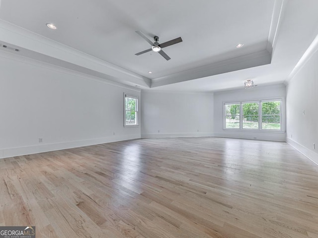 empty room with a tray ceiling, crown molding, healthy amount of natural light, light wood-type flooring, and recessed lighting