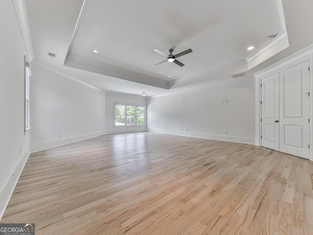 unfurnished living room with a raised ceiling, ornamental molding, a ceiling fan, light wood-style flooring, and baseboards