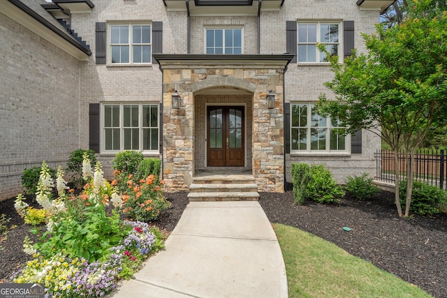 doorway to property featuring french doors, fence, and stone siding