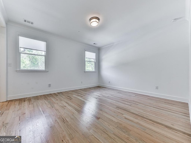 spare room with crown molding, light wood-style floors, and baseboards