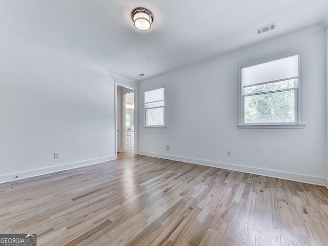 spare room featuring healthy amount of natural light, light wood-style flooring, baseboards, and crown molding