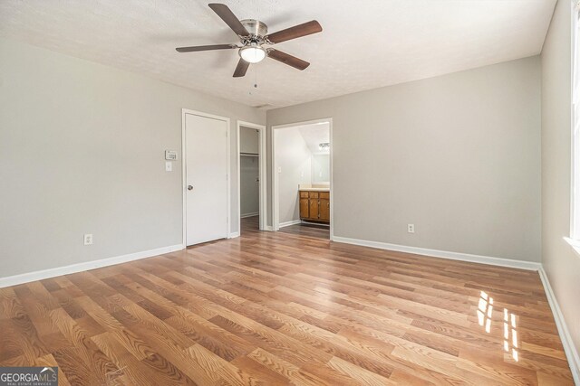 unfurnished bedroom featuring light wood-type flooring, baseboards, a ceiling fan, ensuite bath, and a walk in closet