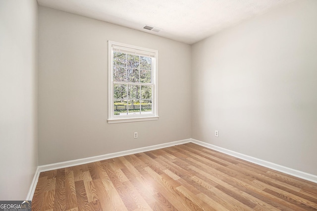 empty room with light wood-style floors, visible vents, and baseboards