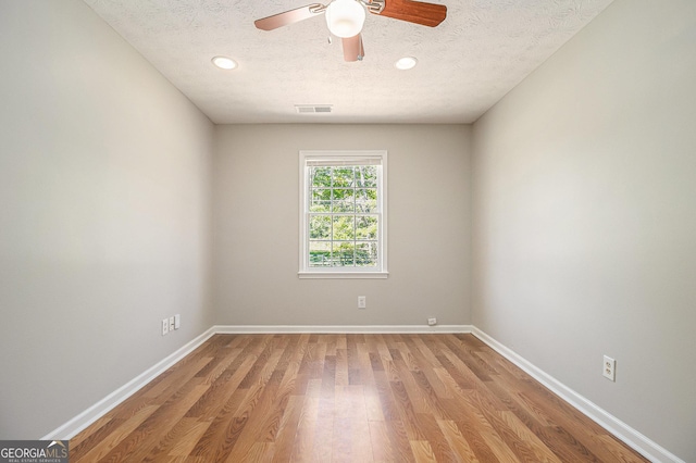 spare room featuring light wood-type flooring, a ceiling fan, visible vents, and a textured ceiling