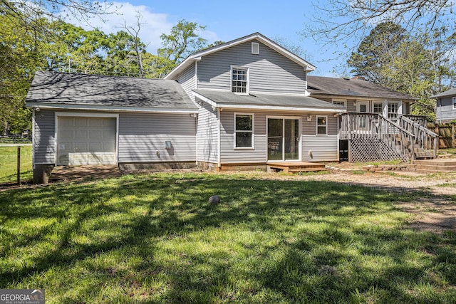 rear view of house with an attached garage, a lawn, and a deck