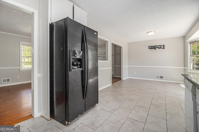 kitchen with white cabinets, black fridge, visible vents, and light tile patterned floors
