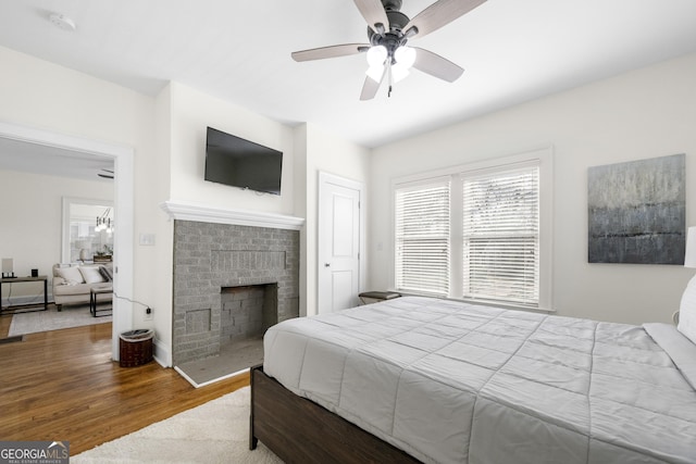 bedroom with ceiling fan, a brick fireplace, and wood finished floors