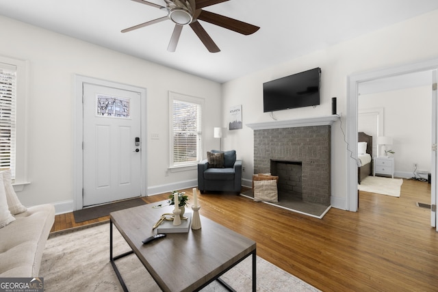 living room with visible vents, baseboards, a ceiling fan, wood finished floors, and a brick fireplace