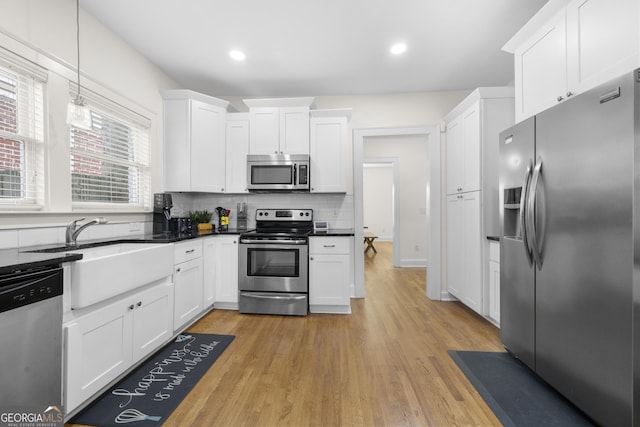 kitchen featuring dark countertops, white cabinetry, stainless steel appliances, and light wood finished floors