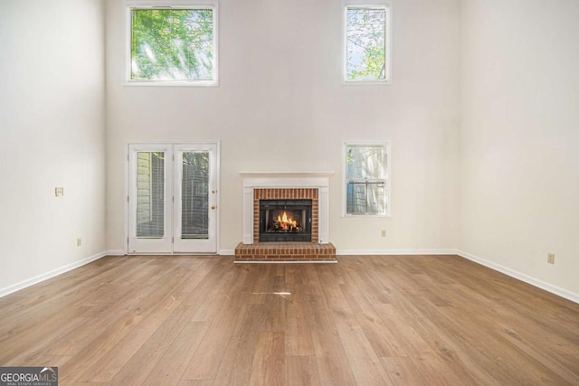 unfurnished living room featuring a wealth of natural light, light wood-style floors, a high ceiling, and a fireplace